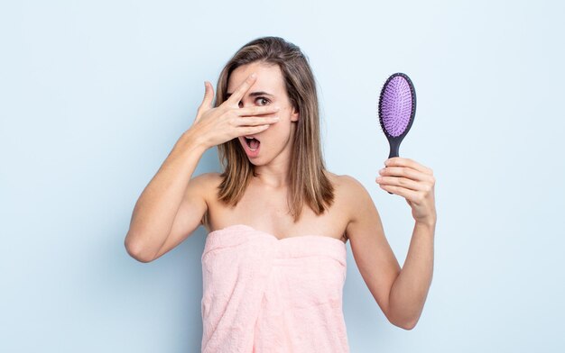 Jeune jolie femme ayant l'air choquée, effrayée ou terrifiée, couvrant le visage avec la main. concept de brosse à cheveux