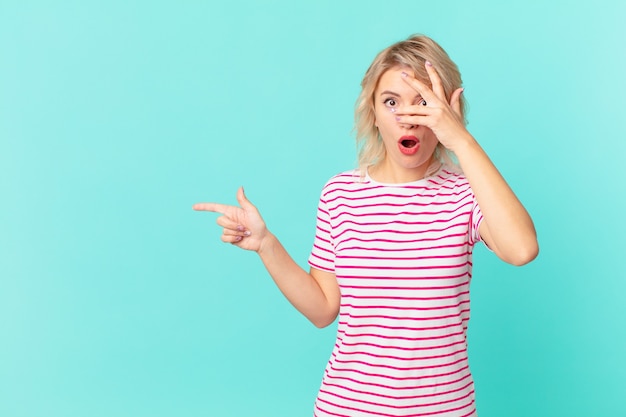 Jeune jolie femme ayant l'air choquée, effrayée ou terrifiée, couvrant le visage avec la main. concept d'espace de copie