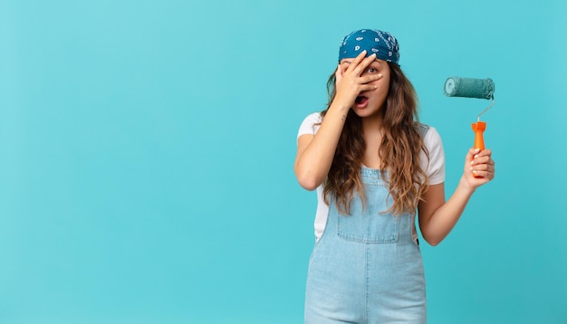 Jeune jolie femme ayant l'air choquée, effrayée ou terrifiée, couvrant le visage avec la main et peignant un mur