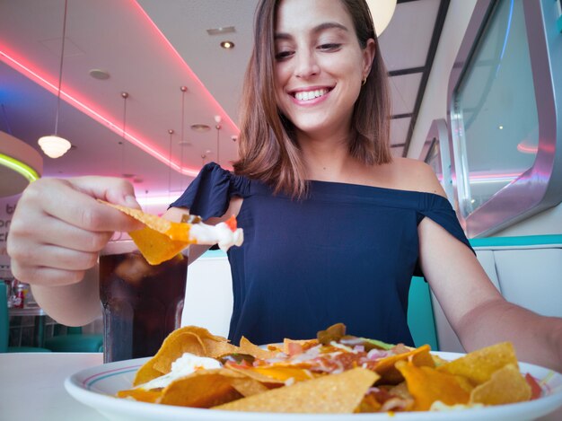 Jeune jolie femme ayant une assiette de nachos au fromage