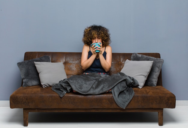 Jeune jolie femme ayant une tasse de café assis sur un canapé