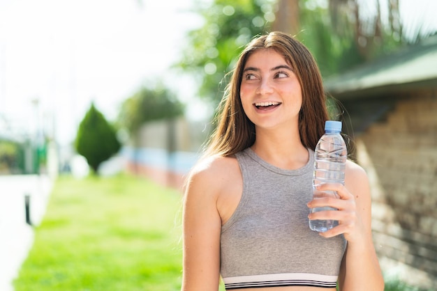 Une jeune et jolie femme blanche avec une bouteille d'eau à l'extérieur regardant en souriant