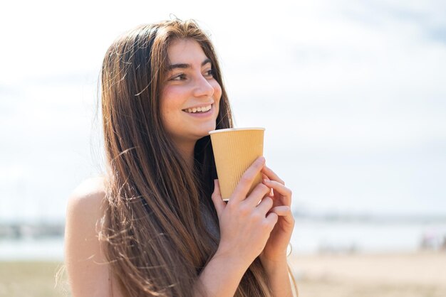 Une jeune et jolie femme blanche tenant un café à emporter.