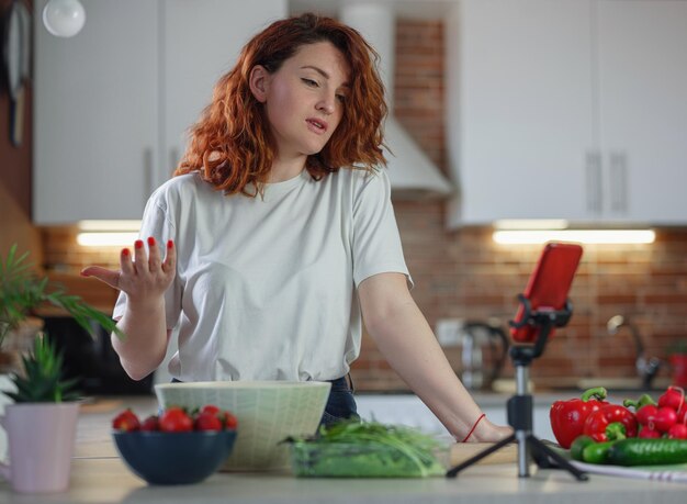 Jeune jolie femme blogueuse tourne une vidéo d'une recette de salade sur un appareil photo de smartphone