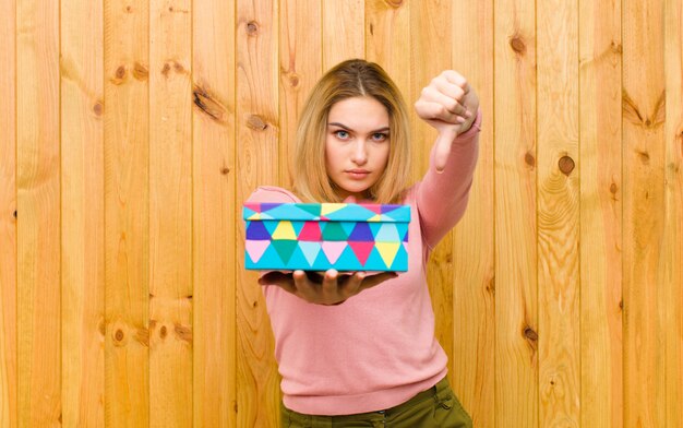 Jeune jolie femme blonde avec une boîte-cadeau contre un mur en bois