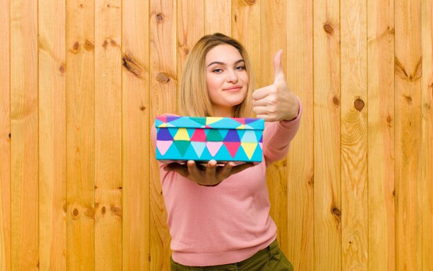 Jeune jolie femme blonde avec un coffret contre un mur en bois