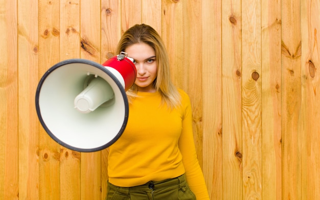 Photo jeune jolie femme blonde avec un mégaphone contre un mur en bois