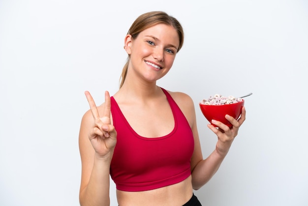 Jeune jolie femme blonde prenant du lait de petit déjeuner isolé sur fond blanc souriant et montrant le signe de la victoire