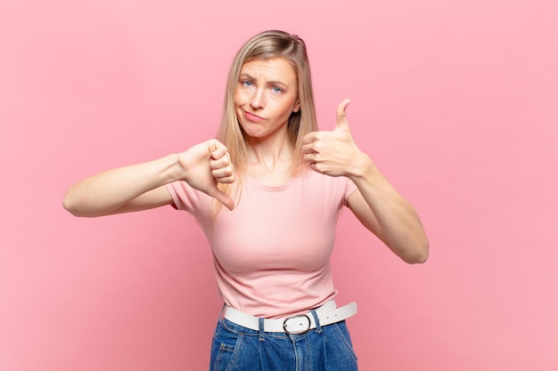 Jeune jolie femme blonde se sentant confuse, désemparée et incertaine, pondérant le bien et le mal dans différentes options ou choix