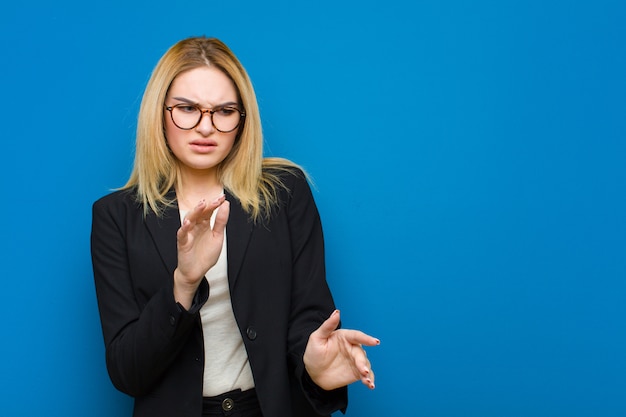 Jeune jolie femme blonde se sentant dégouté et nauséeux s'éloignant de quelque chose de méchant malodorant ou puant disant beurk contre un mur plat