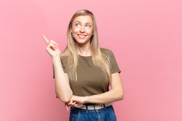 Jeune jolie femme blonde souriant joyeusement et regardant de côté en se demandant de penser ou d'avoir une idée