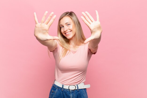 Jeune jolie femme blonde souriante et semblant amicale, montrant le numéro dix ou dixième avec la main vers l'avant, compte à rebours