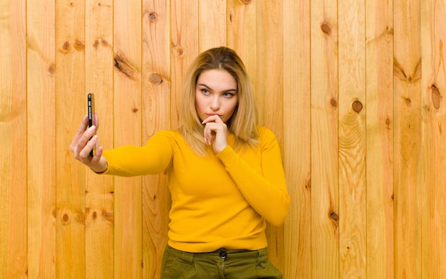 Jeune jolie femme blonde avec un téléphone portable contre le mur en bois