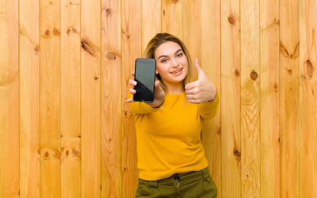 Jeune jolie femme blonde avec un téléphone portable contre un mur en bois