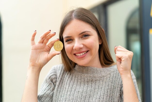 Jeune jolie femme blonde tenant un Bitcoin et célébrant une victoire