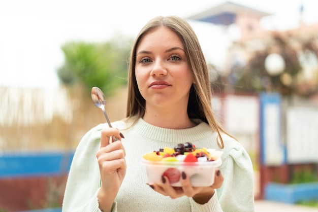 Jeune jolie femme blonde tenant un bol de fruits à l'extérieur