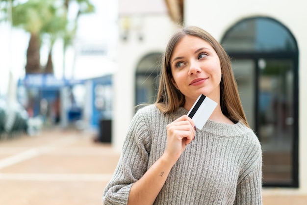 Jeune jolie femme blonde tenant une carte de crédit et pensant