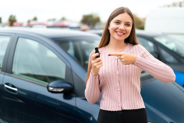 Jeune jolie femme blonde tenant des clés de voiture à l'extérieur et le pointant