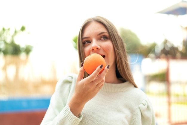 Jeune jolie femme blonde tenant une orange avec une expression heureuse