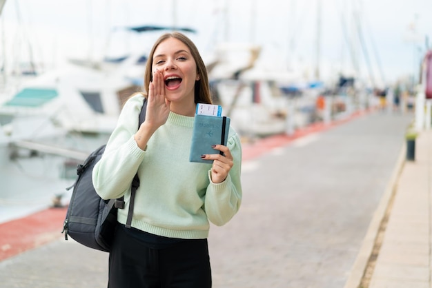 Jeune jolie femme blonde tenant un passeport à l'extérieur en criant avec la bouche grande ouverte