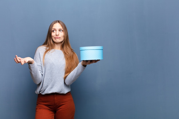 Jeune jolie femme avec une boîte bleue contre un mur bleu avec un espace de copie