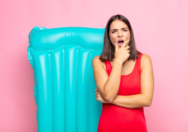 Jeune jolie femme avec la bouche et les yeux grands ouverts et la main sur le menton, se sentant désagréablement choquée, disant quoi ou wow