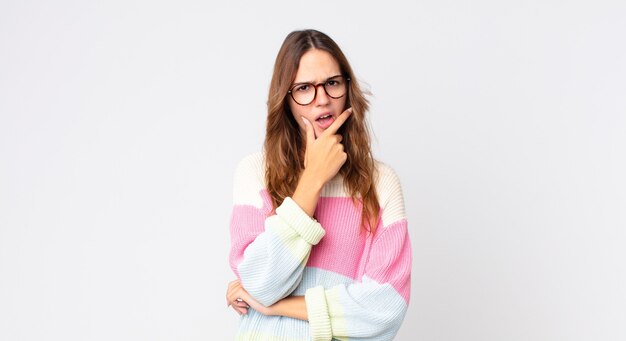 Jeune jolie femme avec la bouche et les yeux grands ouverts et la main sur le menton