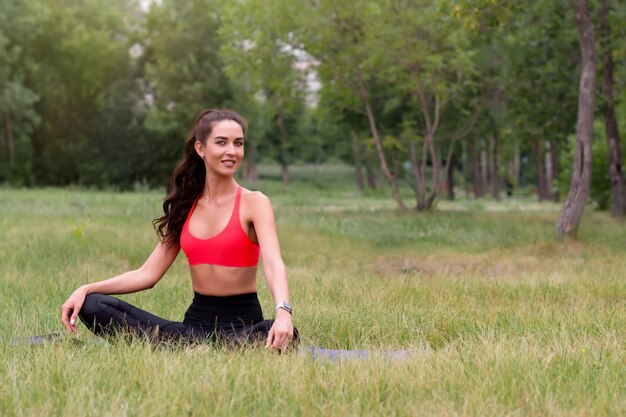 Jeune jolie femme brune tonique souriante faisant du yoga à l'extérieur