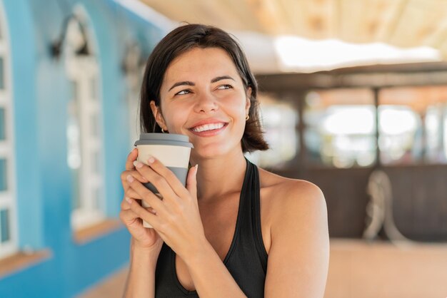 Jeune jolie femme bulgare à l'extérieur tenant un café à emporter et ayant des doutes