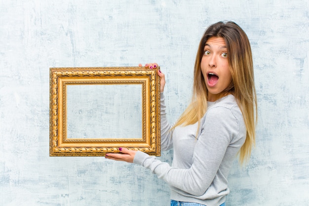 Jeune jolie femme avec un cadre baroque contre le mur de grunge