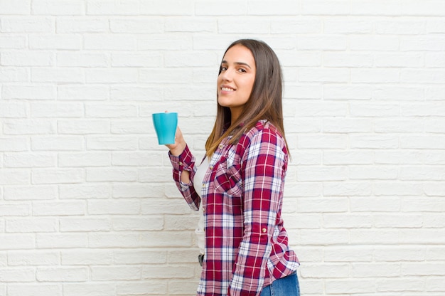 Jeune jolie femme avec un café contre la texture de mur de briques