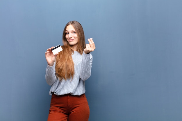 Jeune jolie femme avec une carte de crédit contre un mur bleu avec un espace de copie