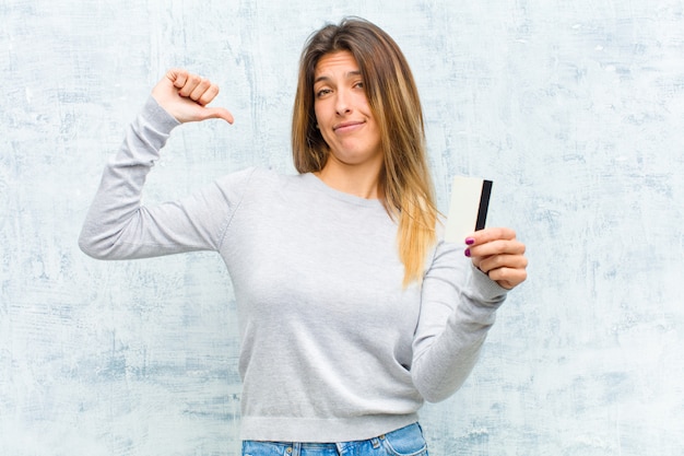 Jeune jolie femme avec une carte de crédit contre le mur de grunge