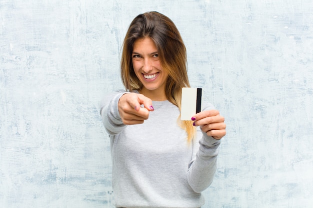 Jeune jolie femme avec une carte de crédit contre le mur de grunge