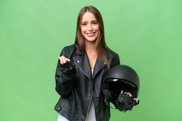 Jeune jolie femme caucasienne avec un casque de moto sur fond isolé faisant un geste d'argent