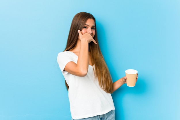 Jeune jolie femme caucasienne tenant un café à emporter montrant un geste d'appel de téléphone mobile avec les doigts.