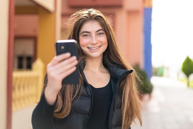 Une jeune et jolie femme caucasienne utilisant un téléphone portable à l'extérieur avec une expression heureuse