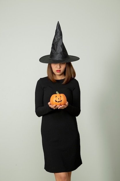 Jeune jolie femme avec chapeau de sorcière tenant halloween citrouille jack o lantern décor