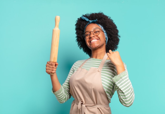 Jeune jolie femme chef afro avec un rouleau à pâtisserie et des pizzas