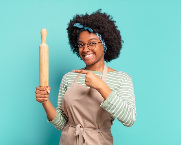 Jeune jolie femme chef afro avec un rouleau à pâtisserie