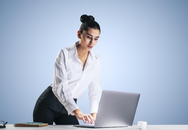 Jeune jolie femme en chemise blanche tapant sur un clavier d'ordinateur portable moderne isolé sur fond de mur bleu clair abstrait gros plan