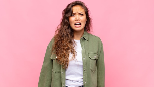 Photo jeune jolie femme avec une chemise ouverte en jean vert posant sur un mur rose