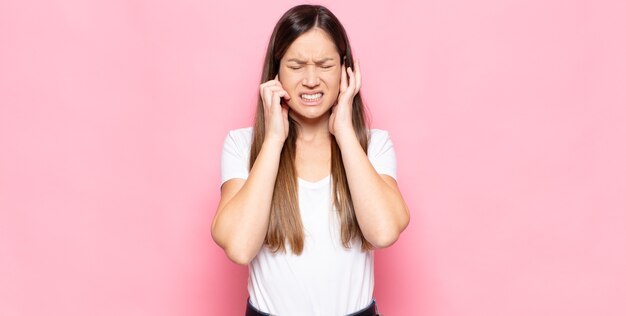 Jeune jolie femme à la colère, stressée et agacée, couvrant les deux oreilles à un bruit assourdissant, un son ou une musique forte