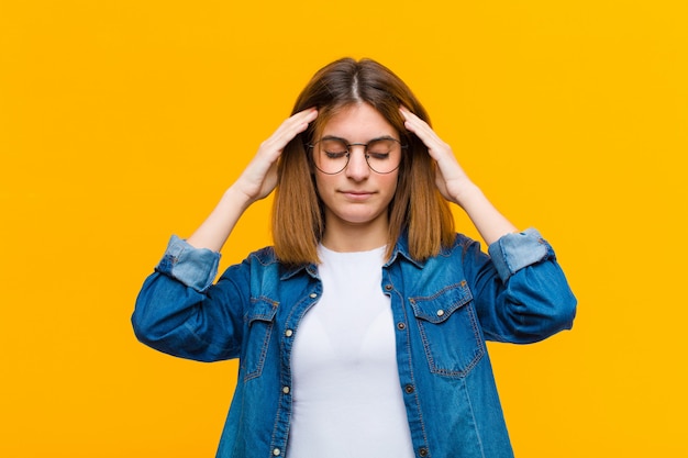 Jeune jolie femme à la concentration, réfléchie et inspirée, remue-méninges et imaginer avec les mains sur le front contre le mur jaune