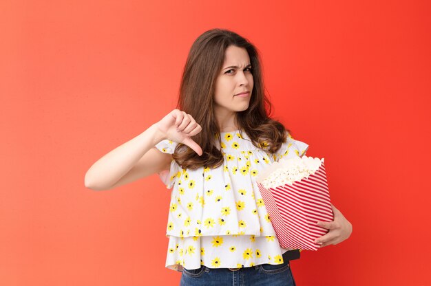 Jeune jolie femme contre un mur rouge avec un seau à pop-corn