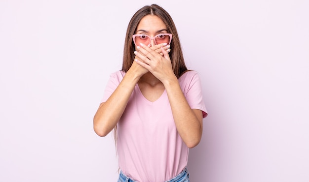 Jeune jolie femme couvrant la bouche avec les mains avec un choc. concept de lunettes de soleil roses