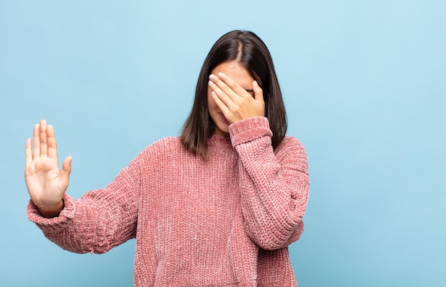 Jeune jolie femme couvrant le visage avec la main et mettant l'autre main à l'avant pour arrêter la caméra, refusant des photos ou des images