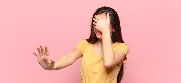 Jeune jolie femme couvrant le visage avec la main et mettant l'autre main devant pour arrêter l'appareil photo, refusant des photos ou des images