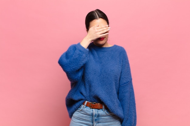 Jeune jolie femme couvrant les yeux d'une main se sentant effrayée ou anxieuse, se demandant ou attendant aveuglément une surprise