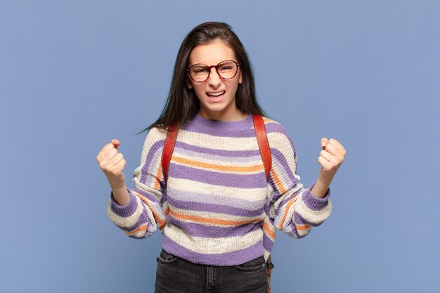 Jeune jolie femme criant agressivement avec un regard agacé, frustré, en colère et des poings serrés, se sentant furieuse. concept d'étudiant